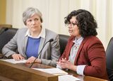 Rinal Ray sits at the testifiers' table and speaks to someone out of view. Representative Pryor sits next to her and watches as she speaks.